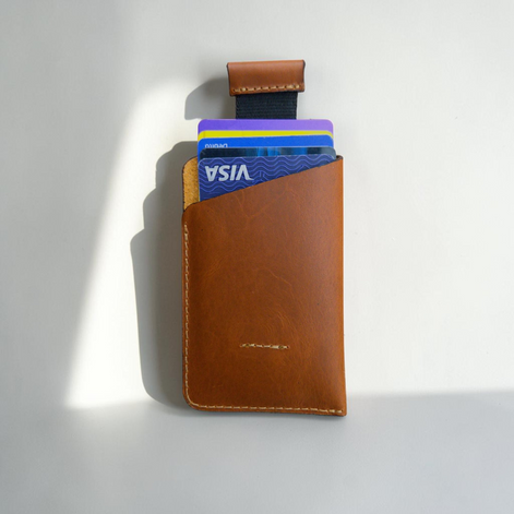 Porta documentos Minimalista Bag de cuero color caramelo con mecanismo de halado para tarjetas sobre fondo de madera